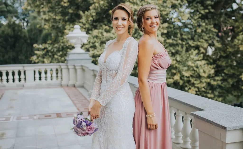 Mother and daughter standing back-to-back, posing for a picture with the mother wearing a Mother of the Groom dress, showing elegance and grace.