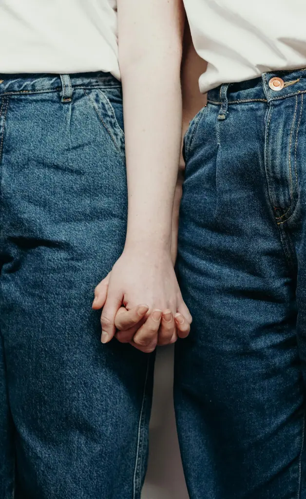 A person wearing jeans is holding hands with someone beside them.