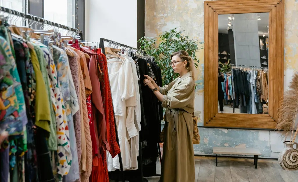 A girl is inspecting clothes hanging on a rack with hangers