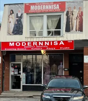 Shop exterior with a black car in front and a banner above displaying women in gowns, wedding dresses, and party dresses on both sides