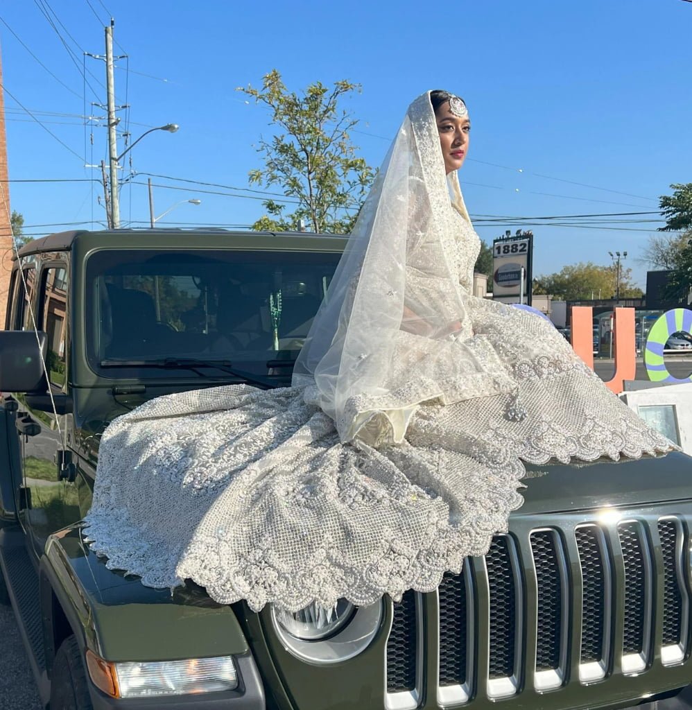 Girl sitting on top of a car in a white wedding dress