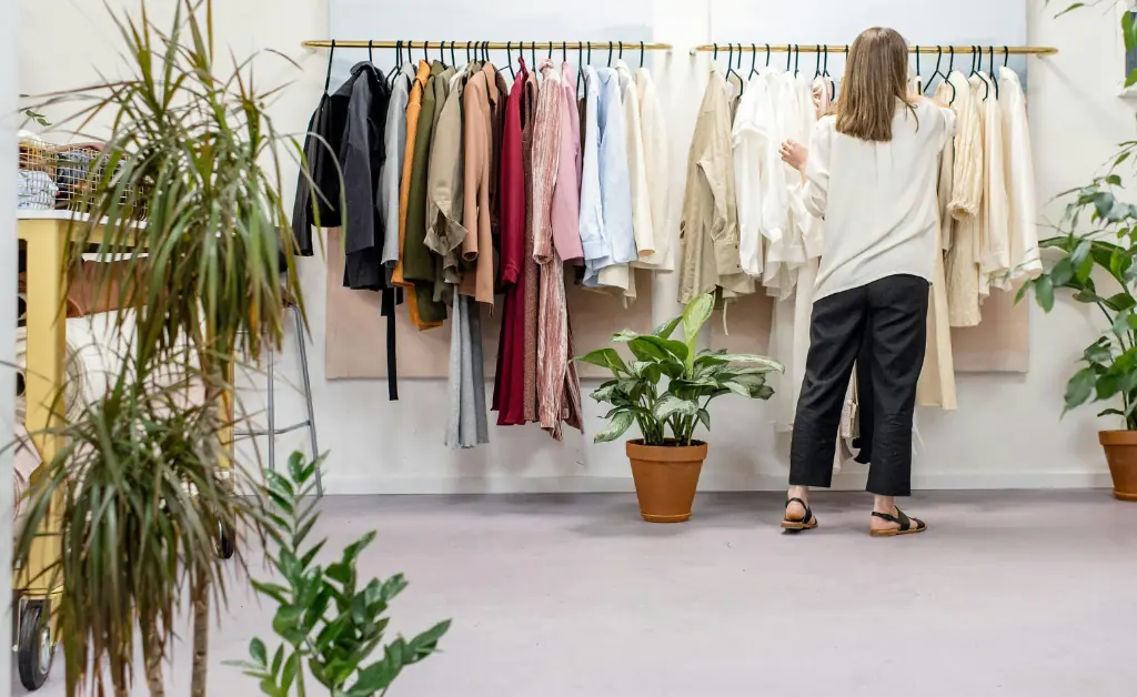 A girl is inspecting clothes hanging on a rack with hangers